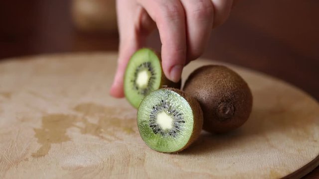 Close-up of the girl puts on the table ripe fruit kiwi. Close-up of ripe sliced kiwi on wooden background. Ripe sliced kiwi on cutting Board, Slow motion.