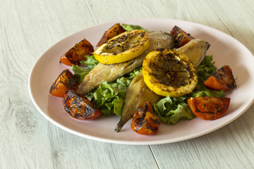 Smoked mackerel fillets with char grilled tomato and lemon on a bed of lettuce with a grey wood background