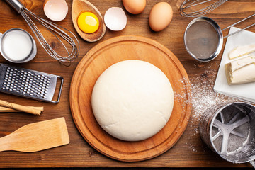Concept for bakery, restaurant, cafe, production. Hands working with dough on a wooden table. Next to the companions, milk, flour, eggs. home made bread, pizza pasta, pies, cakes. copy space, top view