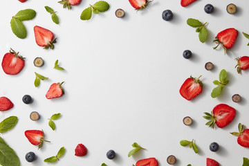 A square frame made of mint leaves, strawberries and blueberries on a gray background. Flat lay