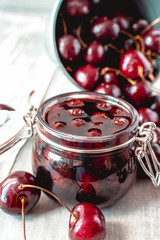 cherry marmalade in a glass jar with a lid, a jar  stands in red cherries, conservation for the winter. selective focus and copy space
