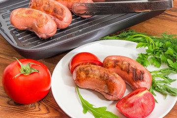 Grilled sausages on dish with greens and tomatoes closeup