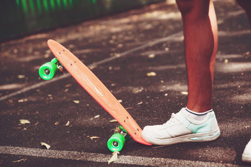 Close up of feet of man sneakers rides on orange penny skateboard on asphalt