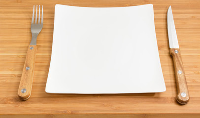 Empty square white dish, fork and knife with wooden handles