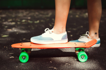 Close up of feet of girl sneakers rides on orange penny skateboard on asphalt