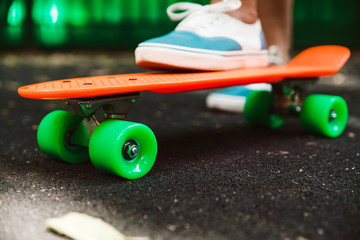 Close up of feet of girl sneakers rides on orange penny skateboard on asphalt