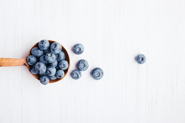 Ripe bluberries in wooden spoon on white wooden table. Top view.