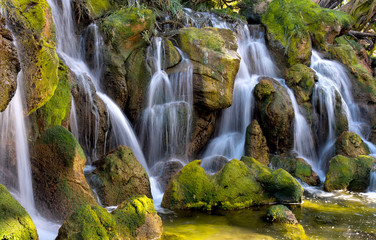Fototapeta na wymiar Waterfall, huge boulders are covered with moss. The stones are flooded with sunlight.