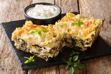 Delicious lasagna with chicken breast, porcini mushrooms, cheese, herbs and bechamel sauce close-up on a slate plate on a wooden table. horizontal - obrazy, fototapety, plakaty