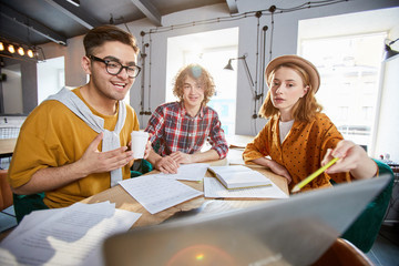 Obraz premium Young businesswoman pointing at data on laptop display while explaining it to colleagues at working meeting