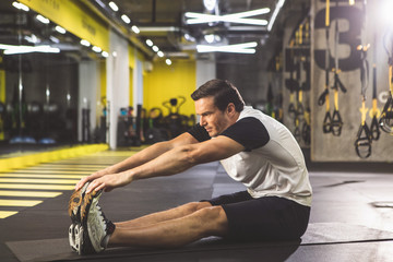Full length side view orderly man doing stretching while sitting on mat in gym