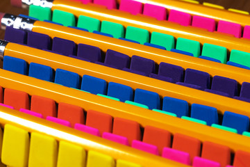 Rows of brightly colored pencil erasers lined up in an OCD orderly fashion, with pencils laying across them. High contrast lighting and high vibrancy , shallow depth of field and a tight framing