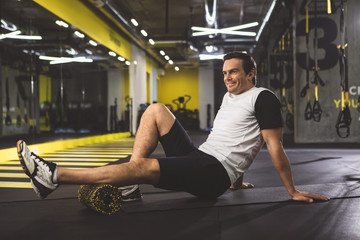 Full length side view beaming man having rest on floor after good training in keep-fit studio