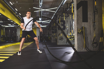 Fototapeta premium Full length portrait of focused man gesticulating hands with special equipment during exercise in gym