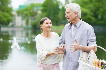 Aged grey-haired man and his wife discussing where to go for picnic in park