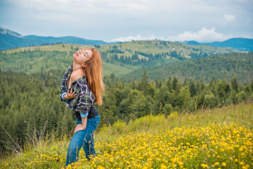 Cheerful woman is having rest on the edge of the cliff and looking at the valley and mountains. Traveling along the mountains, freedom and active lifestyle concept 