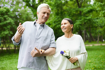 Happy senior couple having talk during promenade in blooming park on summer day © pressmaster