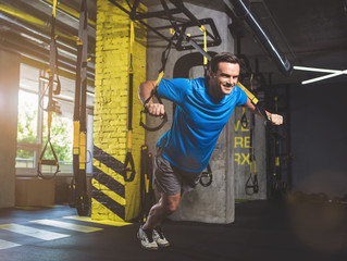 Full length portrait of happy young sportsman taking exercise with trx
