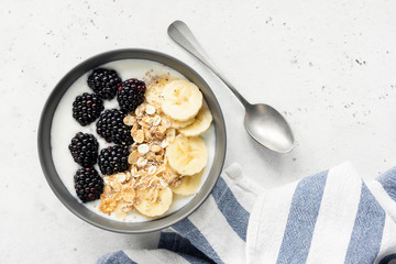 Breakfast smoothie bowl with granola, banana and blackberries on white concrete background, top view