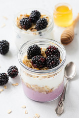 Overnight oats or healthy breakfast parfait with yogurt, granola muesli and blackberries. Closeup view, selective focus
