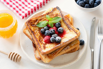 French toast with berries and honey on white plate. Tasty breakfast