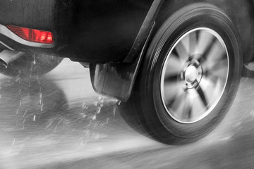 Detail of the rear wheel of a car driving in the rain on a wet road. Aquaplaning in road traffic.