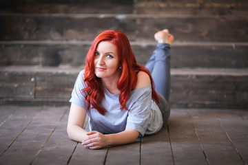 Young woman with red long hair indoor portrait lies on wooden floor
