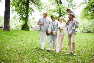 Naklejka na ściany i meble Joyful family of five having talk while walking down green grass in park on summer day