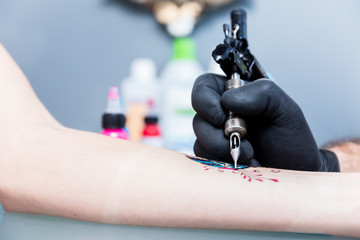 Close-up of the hand of a creative tattoo artist shading a colorful butterfly on the forearm of a female client in a modern studio