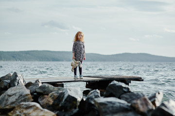 A lonely girl with a plush Bunny is standing on the pier and loo