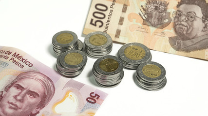 Mexican pesos, stacked coins and bills of various denominations on white background, editorial and illustrative image.