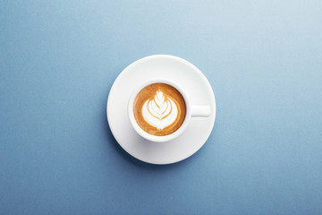 A cup of cappuccino with beautiful latte art on blue background. Top view, central composition. - obrazy, fototapety, plakaty