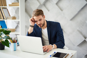 Naklejka premium What should I do. Perplexed man sitting at desktop. He is leaning at hand typing at screen with frustrated look