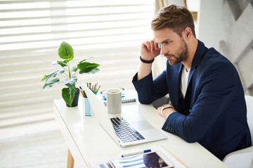 Tough decision. Side view profile of thoughtful male sitting at laptop. He is touching head with...