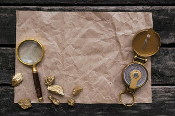 Blank crumpled page with copy space for treasure map, compass, magnifying glass and golden nuggets on old adventure table background.