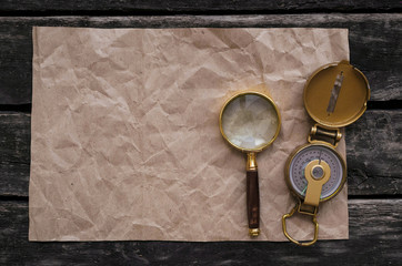 Blank crumpled page with copy space for treasure map, compass and magnifying glass on old adventure table background.