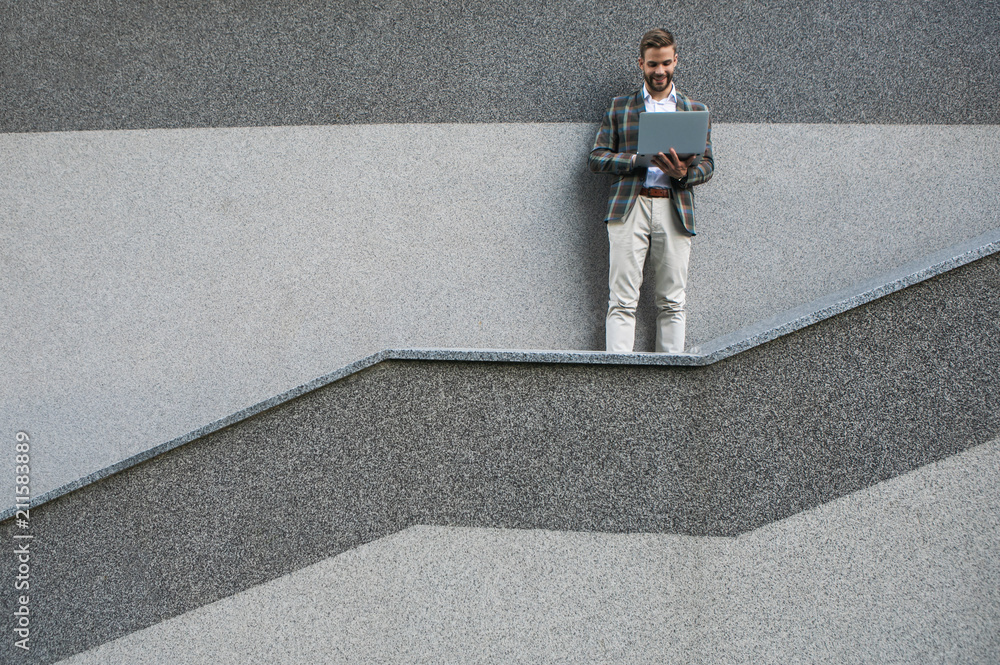 Poster full length portrait of joyful man using notebook computer outdoor. he is standing on contemporary s