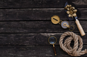 Shovel full of gold ore, compass, rope and magnifying glass on aged wooden table background....