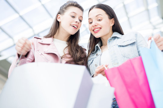 Happy girls looking into paperbags of one another after shopping in contemporary mall on black friday