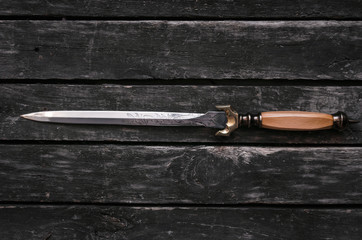 Dagger blade on aged wooden table background with copy space. Assassin weapon.