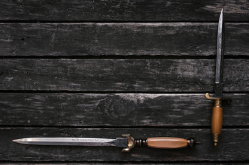 Dagger blade on aged wooden table background with copy space. Assassin weapon.