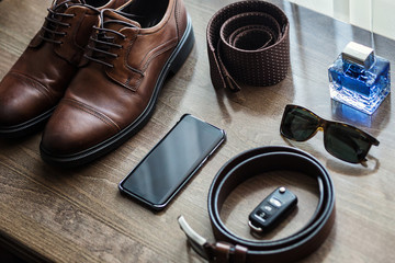 Different men's accessories such as: shoes, belt, tie, glasses, car keys and telephone - are on the table