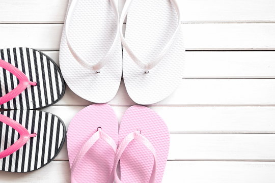 Summer background. Flip-flops on a white wooden background. White, pink, striped beach slippers on light wood. Family vacation. Flat lay, top view, copy space 