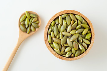 Pumpkin seeds in wooden bowl and spoon on white background