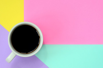 Small white coffee cup on texture background of fashion pastel blue, yellow, violet and pink colors paper in minimal concept