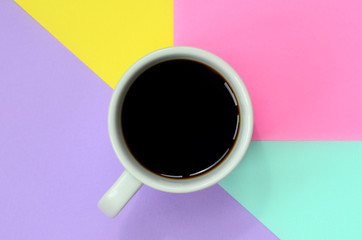 Small white coffee cup on texture background of fashion pastel blue, yellow, violet and pink colors paper in minimal concept