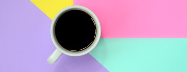 Small white coffee cup on texture background of fashion pastel blue, yellow, violet and pink colors paper in minimal concept