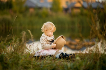 little girl sitting on the lake with a hat