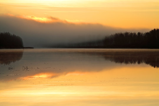 Sun rise colours the sky orange. Lake reflects the same colour. © puteli