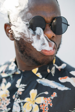 Black stylish man wearing sunglasses. He is vaping with an electronic cigarrete outdoor